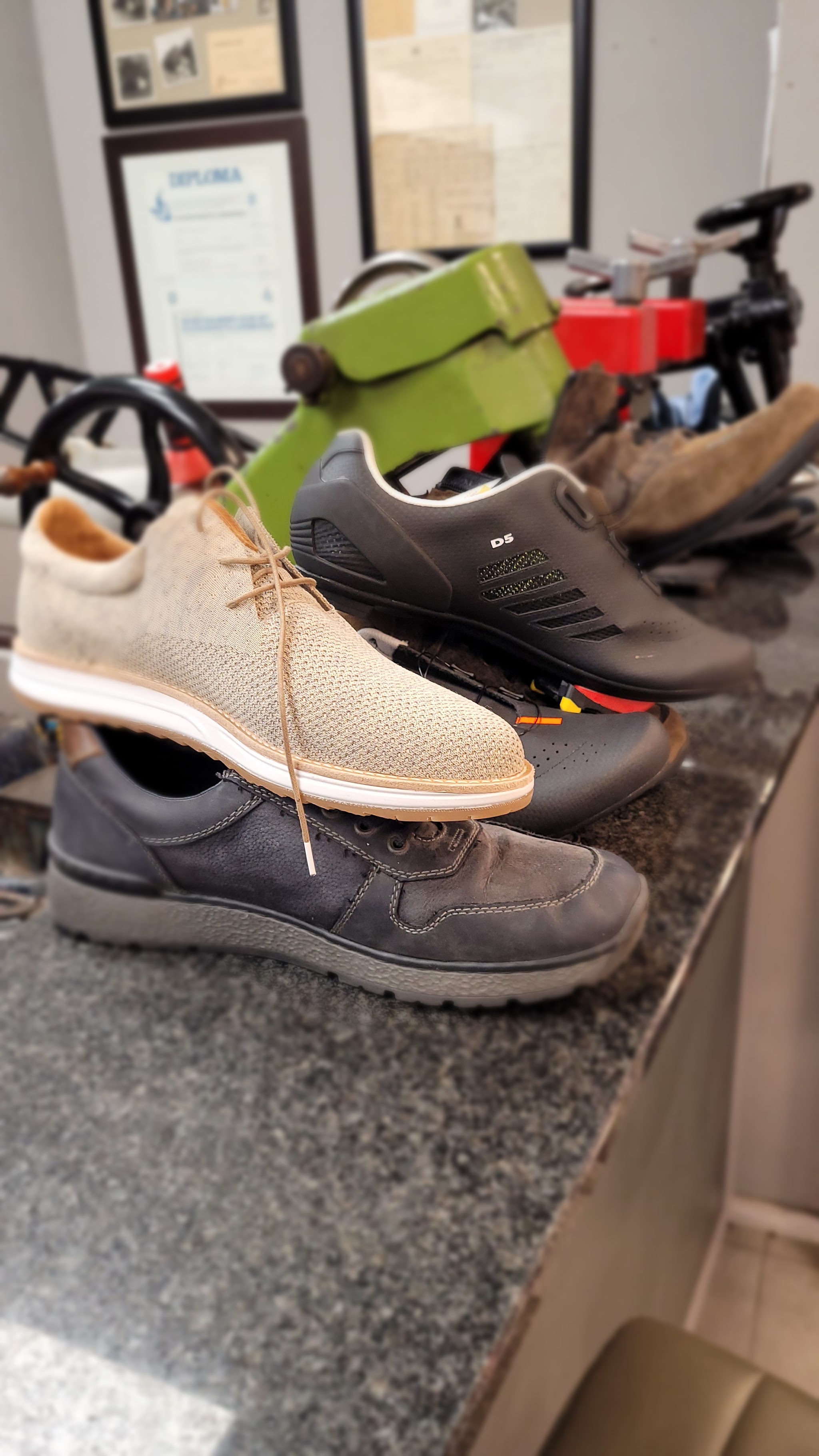 Gerepareerde sneakers en schoenen op de toonbank, met ingelijste diploma's aan de muur